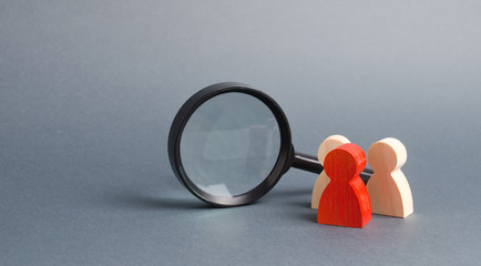 Three wooden human figure stands near a magnifying glass on a gray background. The concept of the search for people and workers. Search for vacancies and work. Human resources, management.
