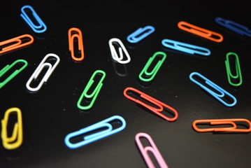 Many bright glossy colorful paper clips lie on a black glossy surface with reflection.