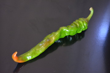Fresh juicy green bitter pepper, chili pepper lying on a black glossy surface with repeated...