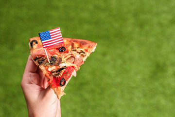 A slice of pizza in female hands with american flag in the form of a toothpick. Lunch on the green...