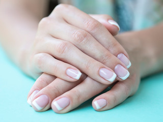 Closeup female french manicure in a beauty salon. Beauty woman nails on a mint background