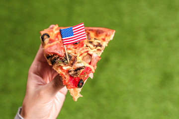 A slice of pizza in female hands with american flag in the form of a toothpick. Lunch on the green...