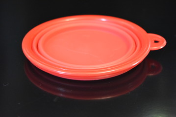 Red folding and multifunctional rubber plate, a bowl with a plastic edging on a black glossy surface.