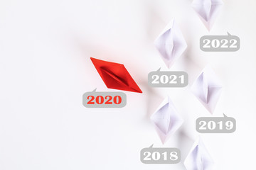The new year 2020 floating away from succession years 2021, 2022. Red paper boat among other white.