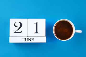 A wooden notebook with a date on June 21 and coffee mug on a blue pastel background. Father's Day.