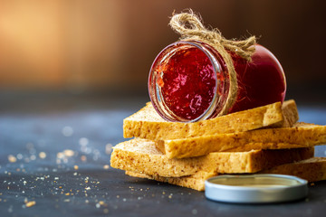 Strawberry jam bottle and whole wheat bread are stacked on a black background. Concept of breakfast and healthy food.