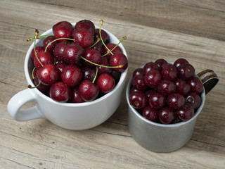 Fresh ripe cherries in cups, on wooden background.