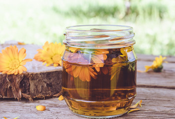 Tincture extract of calendula with fresh flowers in a glass can on a wooden background in nature. Extract of tincture of calendula.