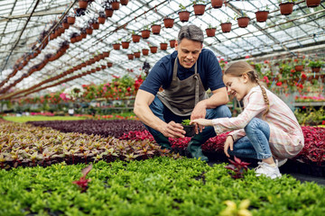 Happy father and daughter taking care of plants in a greenhouse.