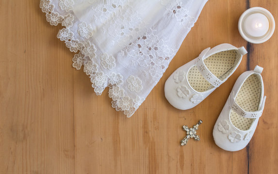 Baptism booties, vintage crhistening dress, candel and crystal pendant on rustic wooden background - top view