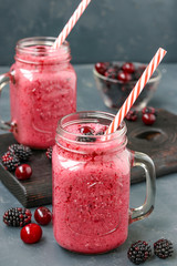 Smoothies with blackberries and cherries in glass on a dark background, vertical orientation
