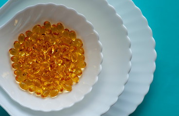 fish oil capsules in a white dish on a blue background