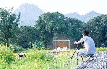 photographer asian men have a mustache, wear glasses. Camera set on the bamboo bridge, photographing the yellow cosmos flower field.