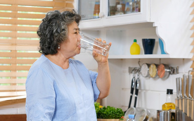 Young beautiful asian woman drinking water while standing by window in kitchen background, people and healthy lifestyles