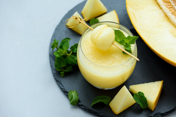 Cold fresh melon smoothie with melon ball and mint leaves on gray wooden background. Summer drink. Healthy food concept. Soft focus