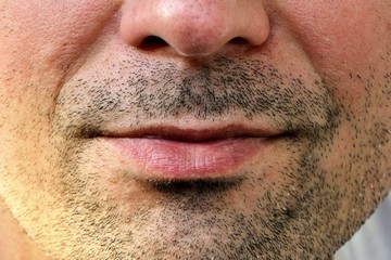 Obraz premium Attractive man with facial hair, mouth and lips with gentle smile, face close up. Sexy smile. Concept of human emotions, skincare. Details of a male face, closeup