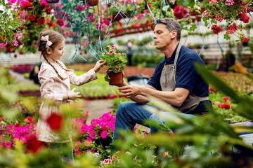 Male florist and his small daughter taking care of flowers at garden center.