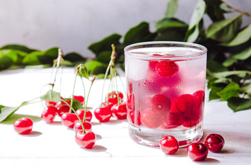 Red cocktail with cherry and ice on a white wooden background. Fresh summer cocktail with cherries and ice cubes.