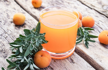 Fresh apricot juice with apricots and twigs of green mint on the background of old boards.