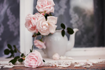   bouquet of pale pink roses in   white teapot vase.