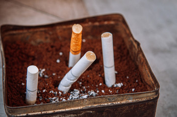 Cigarette filter in old dirty ashtray close up selective focus