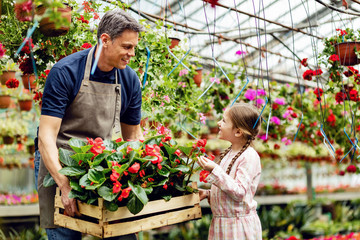 Happy father talking to his daughter while carrying crate with flowers in a greenhouse.