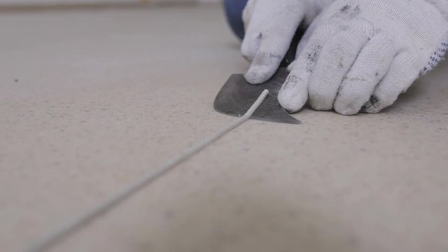 A master linoleum using a month-old knife cuts off the excess welding cord after a hot spike of linoleum
