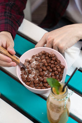 Man is having breakfast with green smoothie and chocolate cornflakes on a terrace