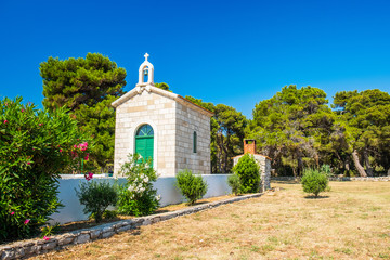 Fototapeta na wymiar Croatia, island of Dugi Otok, beautiful old stone church of Veli Rat on the stone shore among the pines on sunny day, Mediterranean landscape