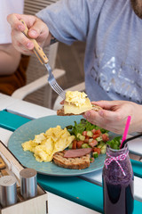 Man is having continental breakfast on a terrace: omelette with salad and toasts with cheese and ham