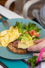 Man is having continental breakfast on a terrace: omelette with salad and toasts with cheese and ham