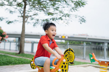 Asian Vietnamese handsome boy sitting on seesaw at outdoor playground