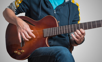 Man playing on classic guitar against silver background. Handsome young men playing guitar