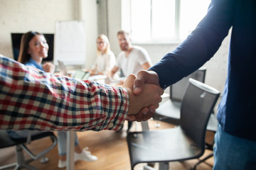 Obraz premium My congratulations! Two cheerful businessmen shaking hands while being in office together with their colleagues.