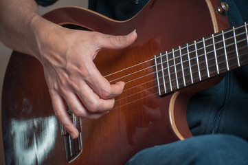 Man playing on classic guitar against silver background. Handsome young men playing guitar