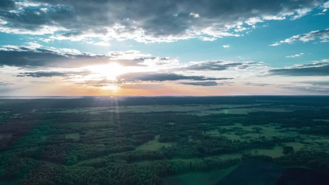 Beautiful sunset sky over a green meadows with mixed forest. agricultural fields with last sunlights shining through the clouds in summer evening. horizon line and sky gradient. countryside landscape