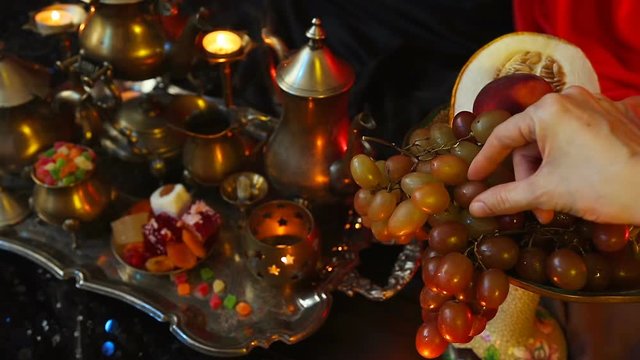 Female hand take Grapes. Traditional Moroccan Sweets on Tray. Teapot and cups of tea with indian snack.