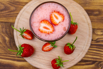 Glass of fresh strawberry smoothie on a wooden table. Top view