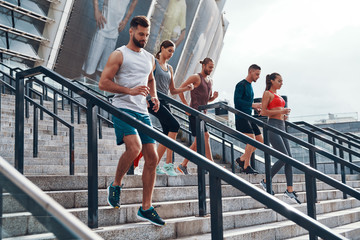Group of young people in sports clothing jogging while exercising on the stairs outdoors