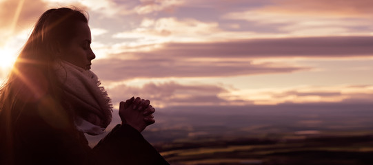 Christian worship and praise. A young woman is praying and worshiping in the evening. - obrazy, fototapety, plakaty