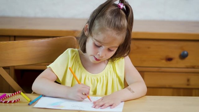 little girl in a yellow dress with crayons draws on paper