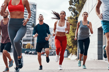 Fototapeta premium Group of young people in sports clothing jogging while exercising on the sidewalk outdoors