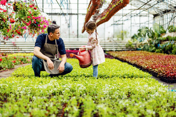Happy little girl and her father watering plants at garden center. © Drazen