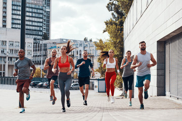 Full length of people in sports clothing jogging while exercising on the sidewalk outdoors