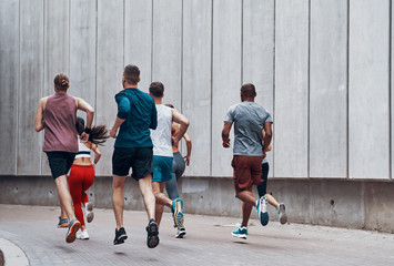 Naklejka premium Full length rear view of people in sports clothing jogging while exercising outdoors