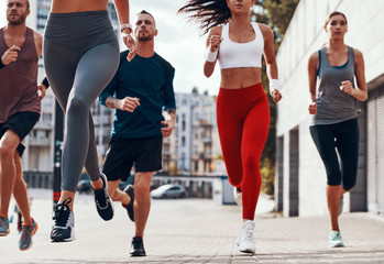 Group of young people in sports clothing jogging while exercising on the sidewalk outdoors