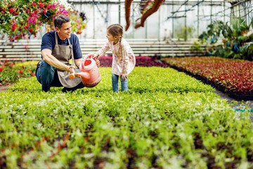 Happy father and daughter talking while watering flowers at plant nursery.