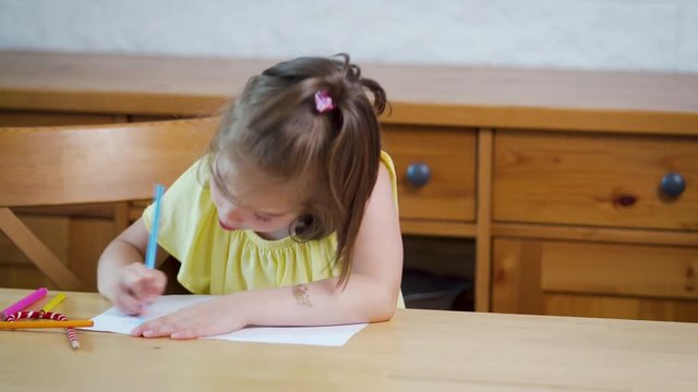 little girl in a yellow dress with crayons draws on paper