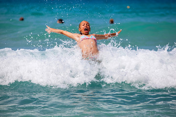 Young girl laughing and crying in the spray of waves at sea on a sunny day..
