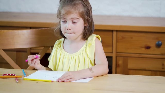 little girl in a yellow dress with crayons draws on paper